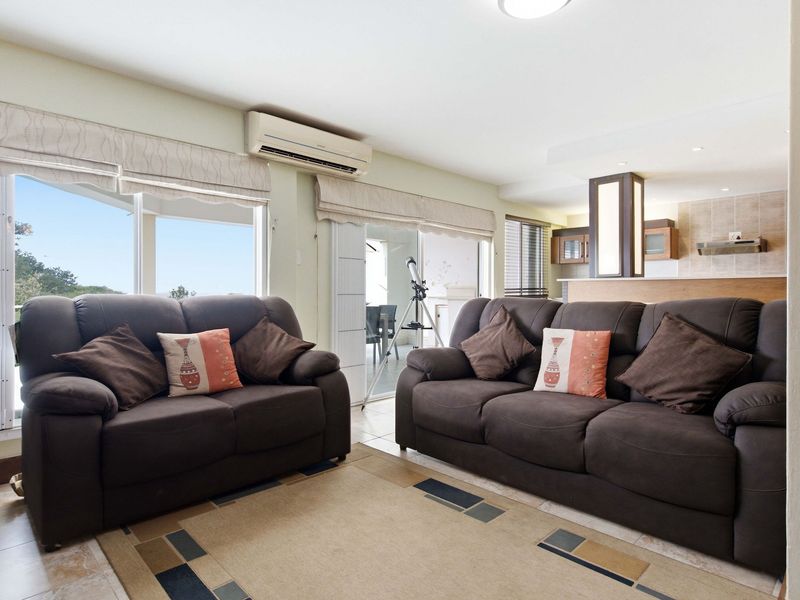 Open-plan living area featuring tiled floors, split-system air conditioning, and seamless flow to an adjoining kitchen with built-in cabinetry and modern finishes.