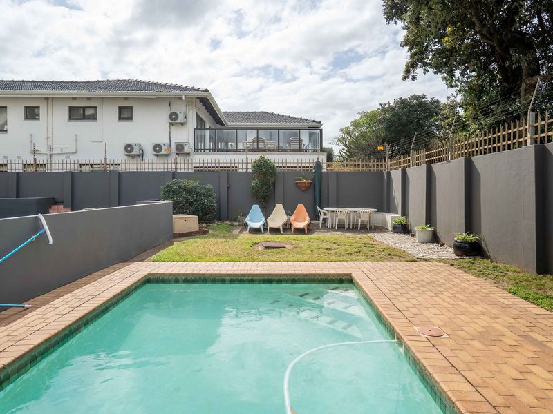 Private outdoor pool area featuring brick paving, a lawned garden, and secure boundary walls with electric fencing.