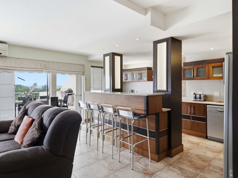 Open-plan living and kitchen area featuring a breakfast bar, tiled flooring, recessed lighting, and direct access to a balcony through sliding glass doors.