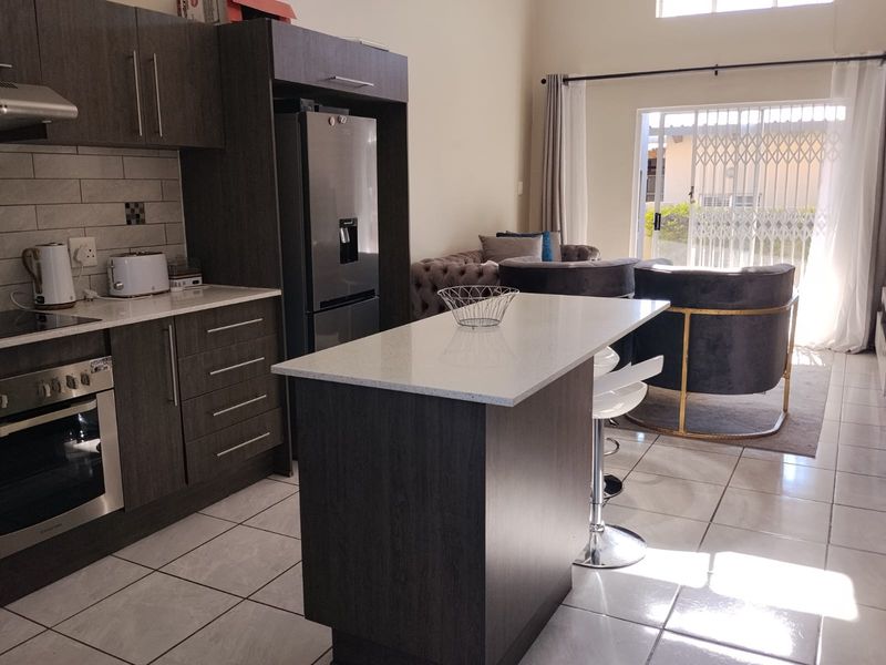 Modern open-plan kitchen and living area featuring dark wood cabinetry, stone countertops, a central island, and direct access to the patio through sliding doors.