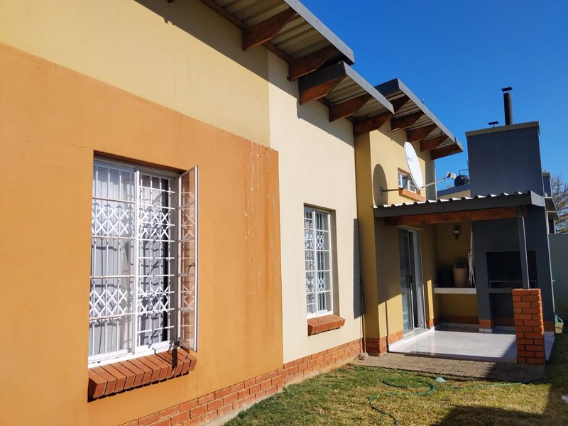 Rear exterior view of the townhouse featuring a tiled patio with a built-in braai, security bars on windows, and exposed timber roof rafters.