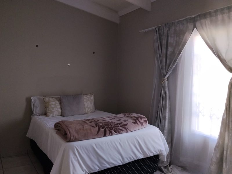 A bedroom featuring tiled flooring and a window with curtain rods. The walls show minor imperfections and exposed wall anchors.