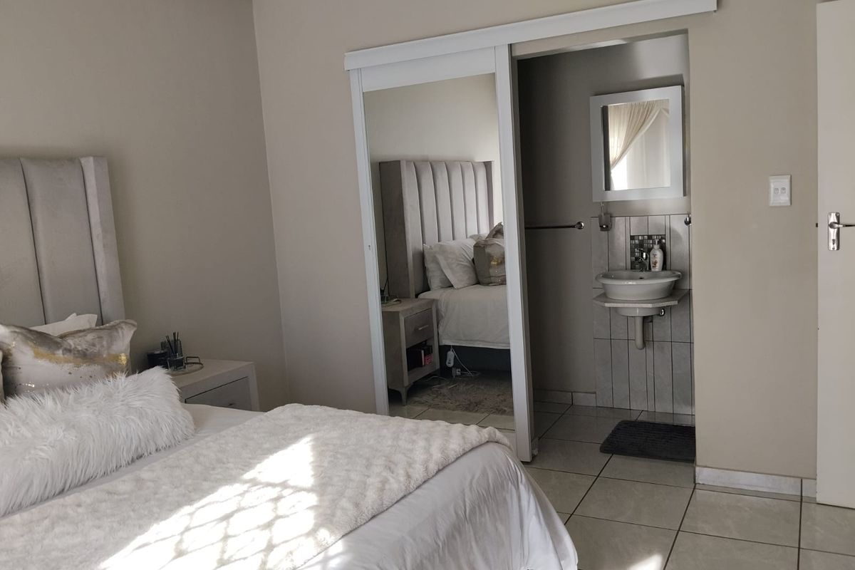 A bedroom featuring tiled flooring, a sliding mirror wardrobe, and an integrated en-suite bathroom area with a wall-mounted basin.