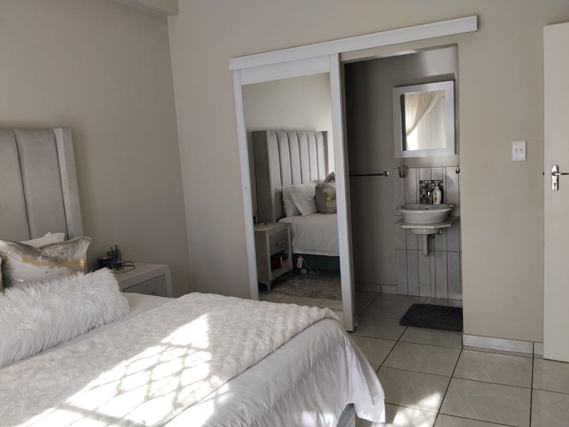 A bedroom featuring tiled flooring, a sliding mirror wardrobe, and an integrated en-suite bathroom area with a wall-mounted basin.