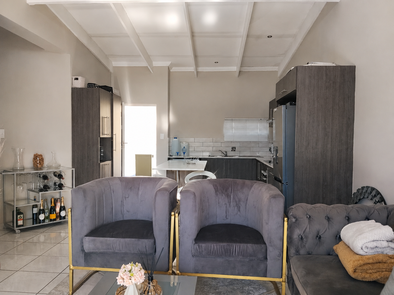 An open-plan living and kitchen area featuring modern dark cabinetry, a subway tile backsplash, and a distinctive exposed beam ceiling with tiled flooring throughout.