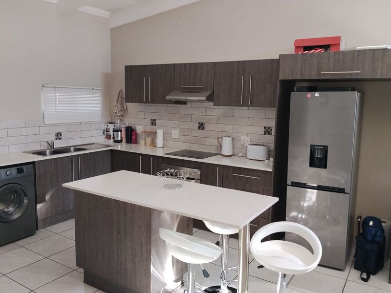 Modern kitchen featuring dark wood cabinetry, stone countertops, subway tile backsplash, a central island, and integrated appliances.