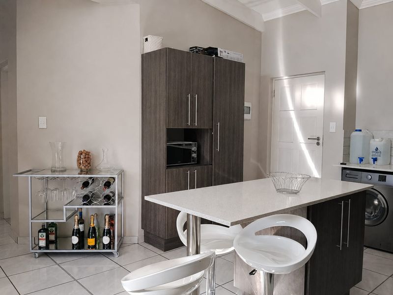 A modern kitchen area featuring dark wood cabinetry, a stone-topped island, and tiled flooring, providing a functional and contemporary prep space.