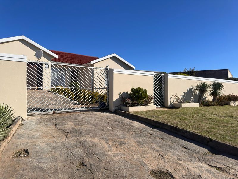 Front exterior view of the property featuring a concrete driveway, perimeter wall, and metal security gates leading to the main entrance.