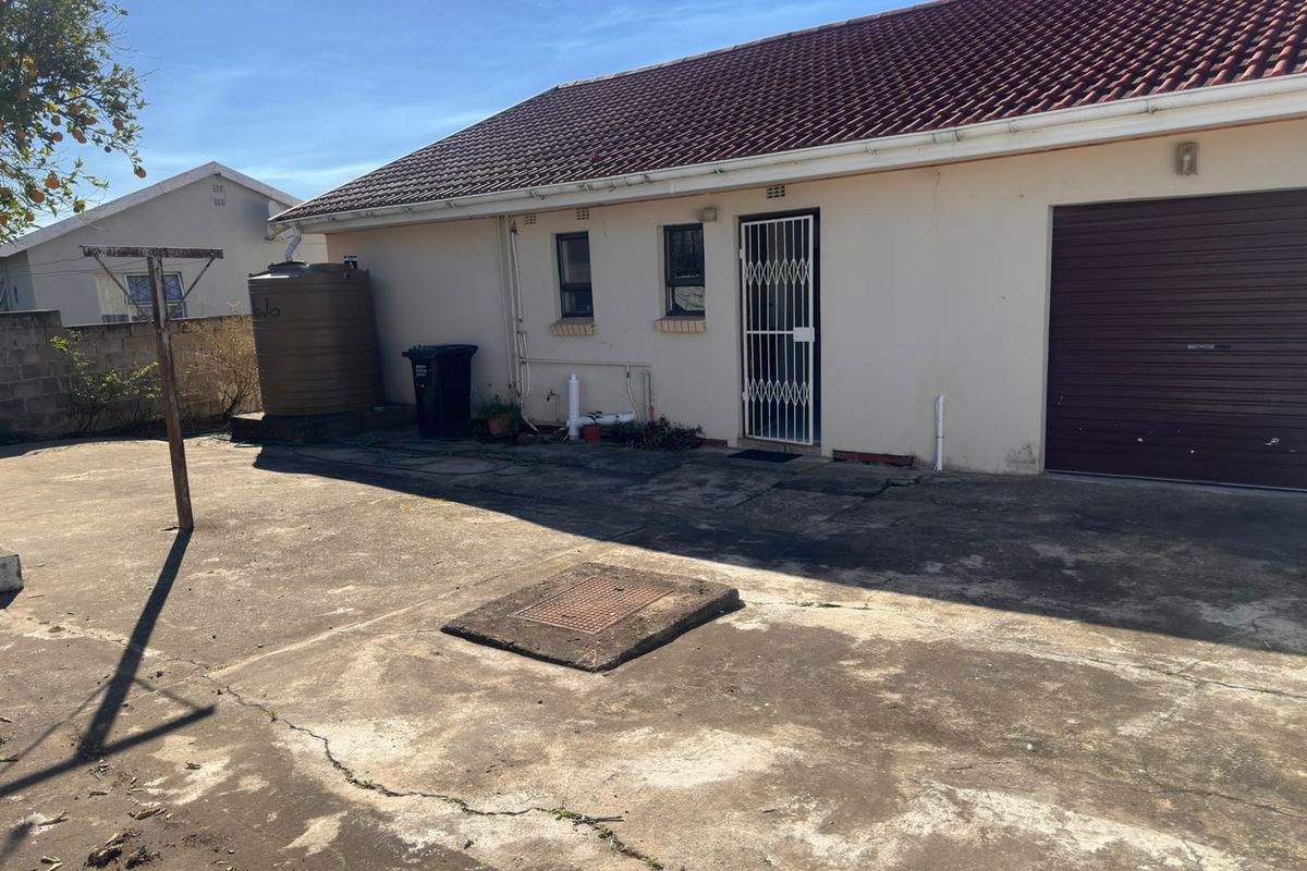 Rear exterior view of the property featuring a concrete paved yard, water storage tank, and access to the garage and side entrance.