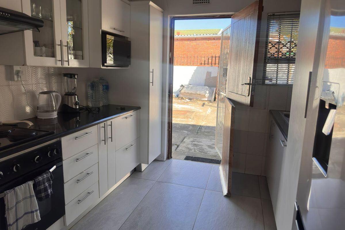 A functional kitchen featuring white cabinetry, black countertops, built-in appliances, and direct access to the rear exterior through a stable door.