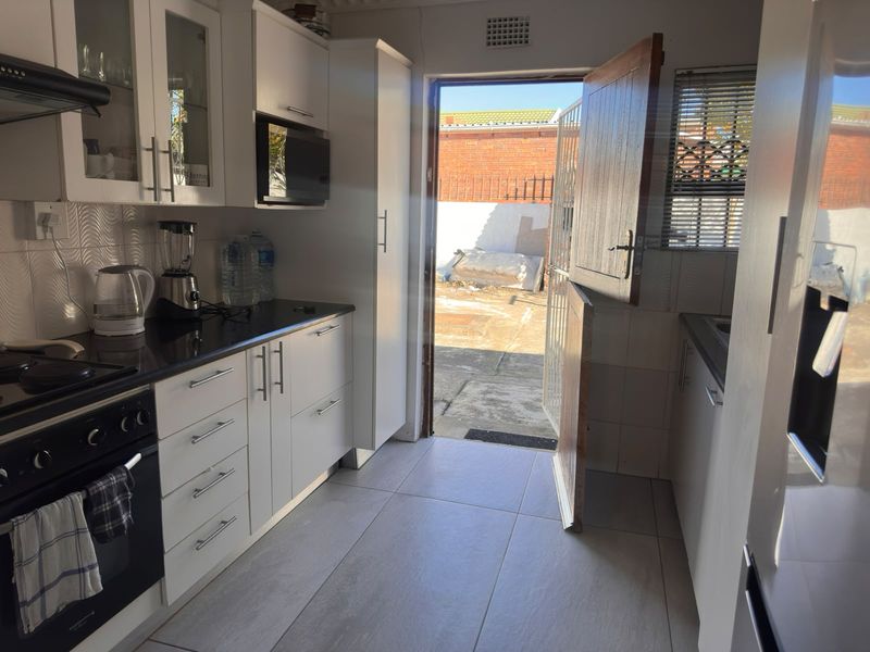 A functional kitchen featuring white cabinetry, black countertops, built-in appliances, and direct access to the rear exterior through a stable door.