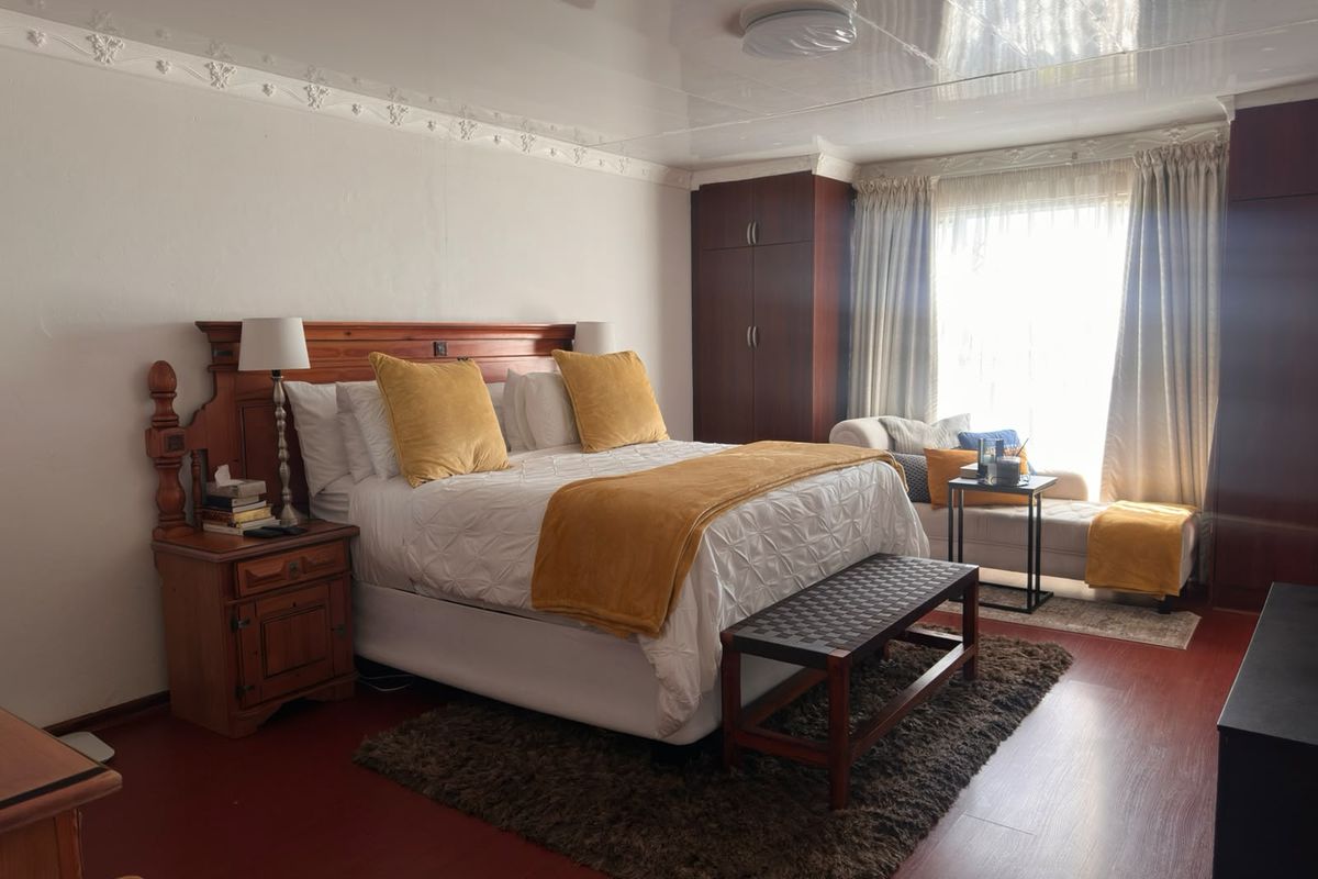 Spacious bedroom featuring built-in wooden cupboards, decorative ceiling cornices, and laminate flooring, offering a comfortable and functional living space.