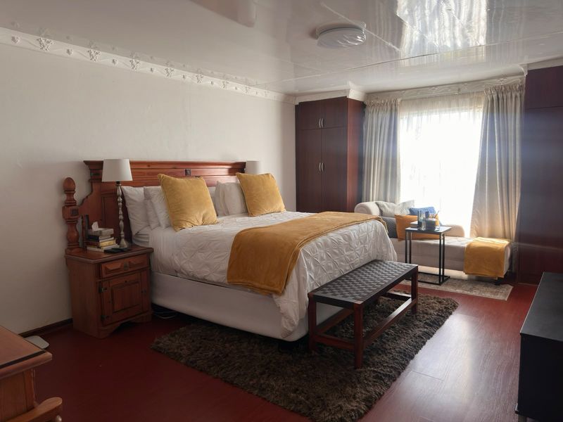 Spacious bedroom featuring built-in wooden cupboards, decorative ceiling cornices, and laminate flooring, offering a comfortable and functional living space.