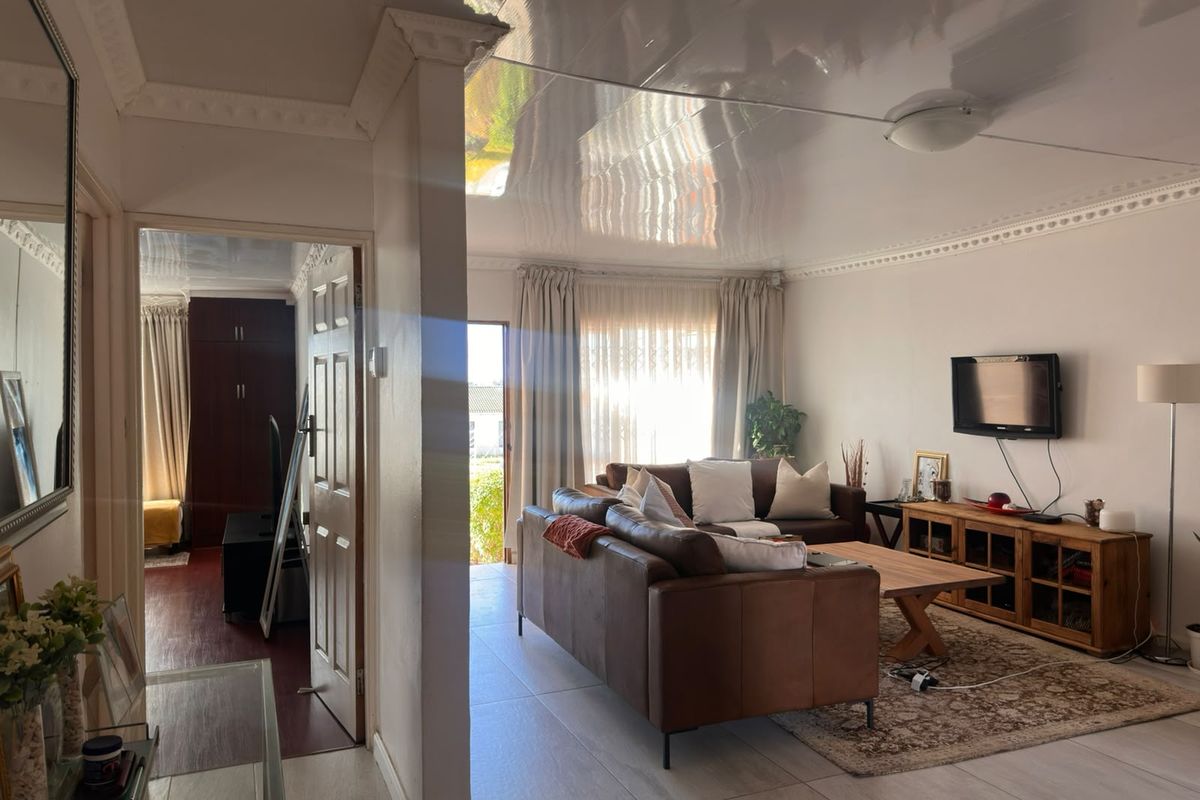 A living room featuring a glossy ceiling, crown molding, and tiled flooring, with an adjacent view into a secondary room.