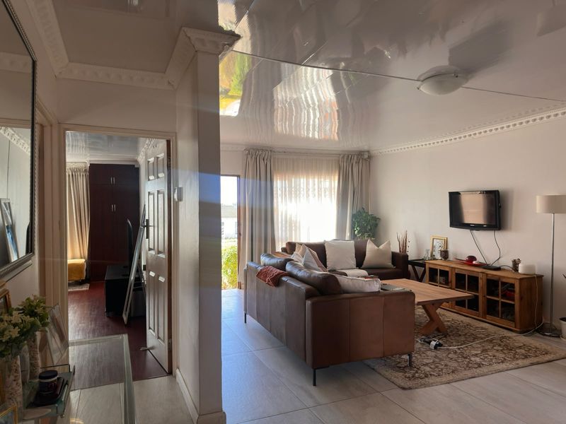 A living room featuring a glossy ceiling, crown molding, and tiled flooring, with an adjacent view into a secondary room.