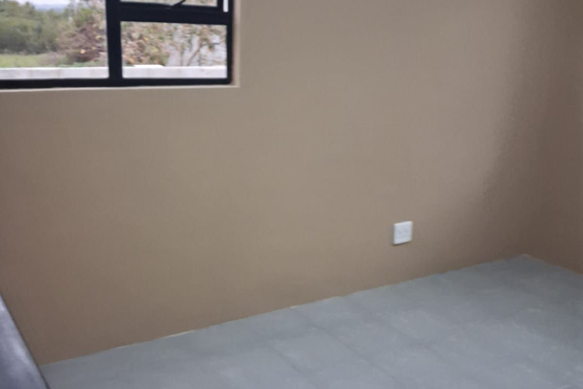 A clean, empty bedroom featuring neutral wall paint, grey tiled flooring, and an aluminium-framed window.
