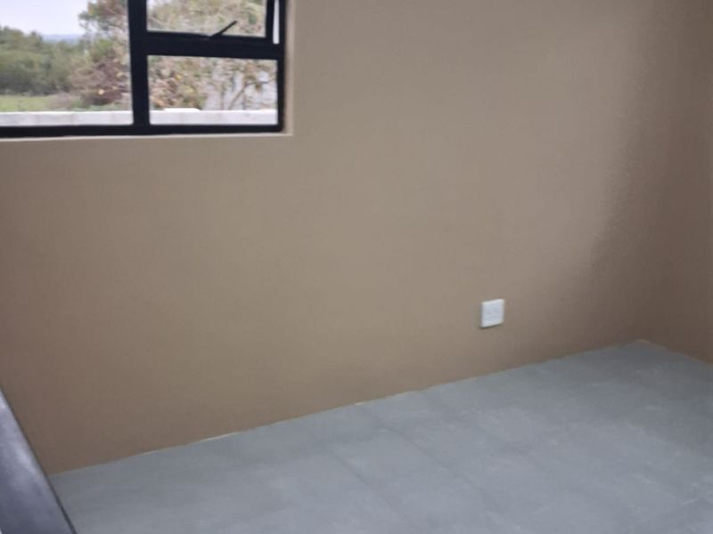 A clean, empty bedroom featuring neutral wall paint, grey tiled flooring, and an aluminium-framed window.