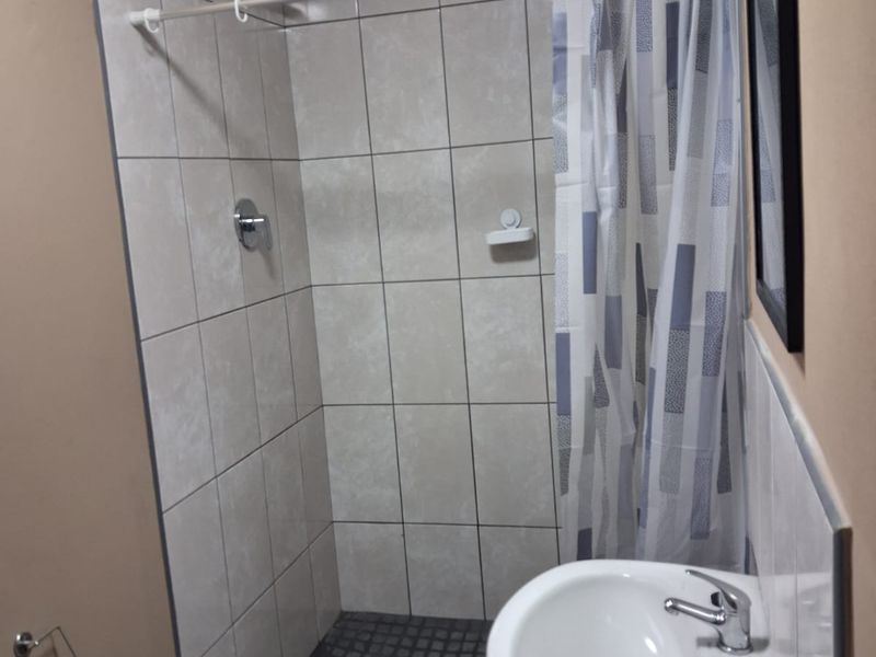 A compact bathroom featuring a tiled shower enclosure with a wall-mounted basin and exposed plumbing.