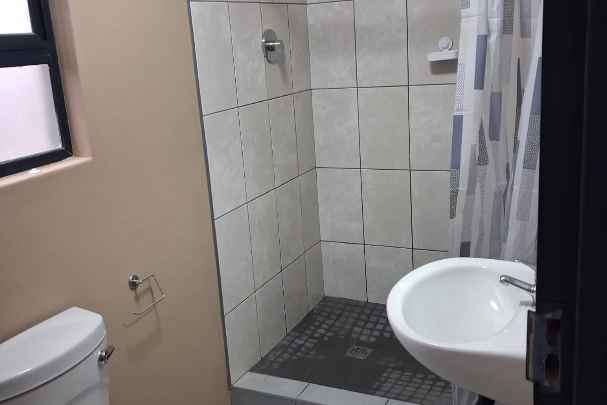 A functional bathroom featuring a tiled shower enclosure, wall-mounted basin, and standard toilet with neutral wall finishes.