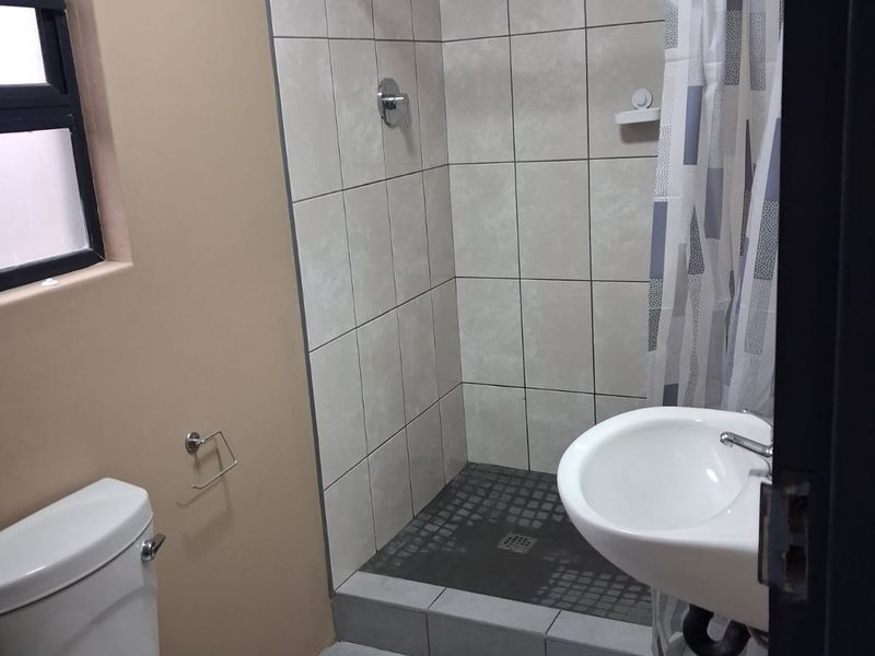 A functional bathroom featuring a tiled shower enclosure, wall-mounted basin, and standard toilet with neutral wall finishes.