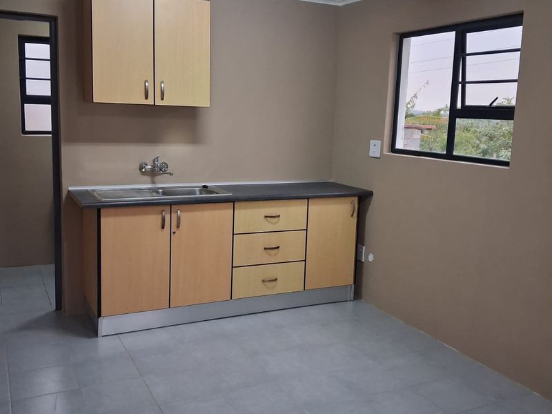 A clean, empty kitchen featuring light wood-tone cabinetry, a stainless steel sink, tiled flooring, and neutral wall finishes.