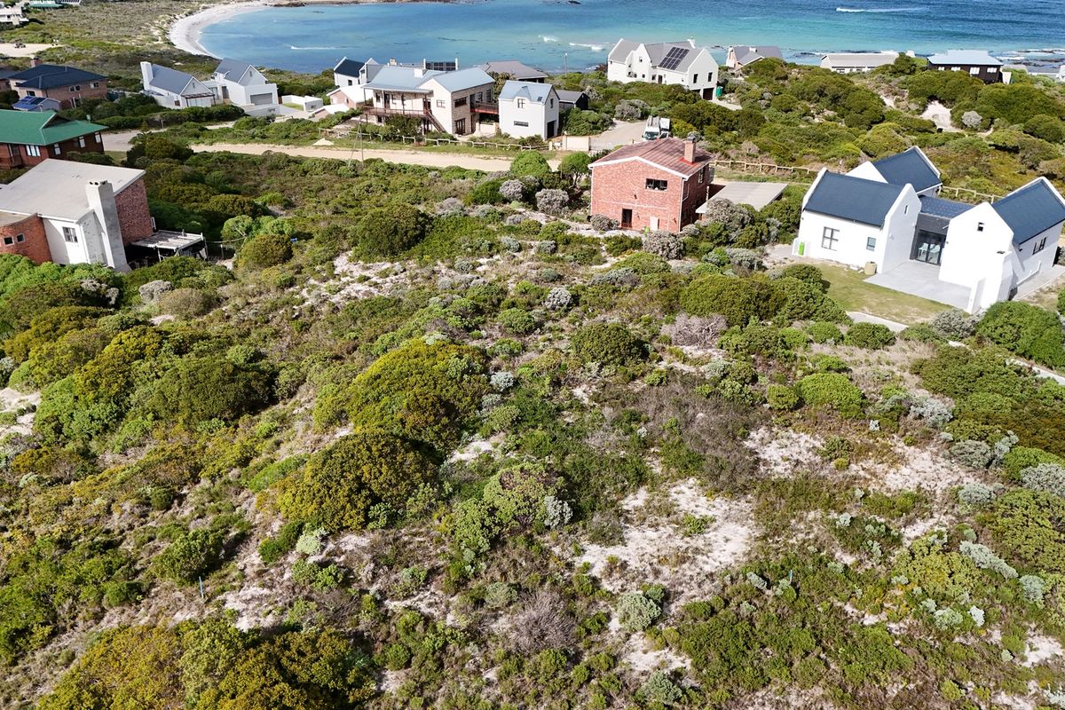 Aerial view of a vacant residential plot featuring natural coastal vegetation and sandy terrain, situated in a developed coastal neighborhood.