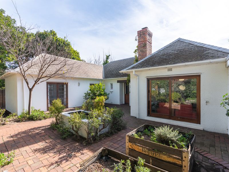 A private rear courtyard featuring brick paving, a raised garden bed, and access to the home through sliding glass doors and a brick chimney.