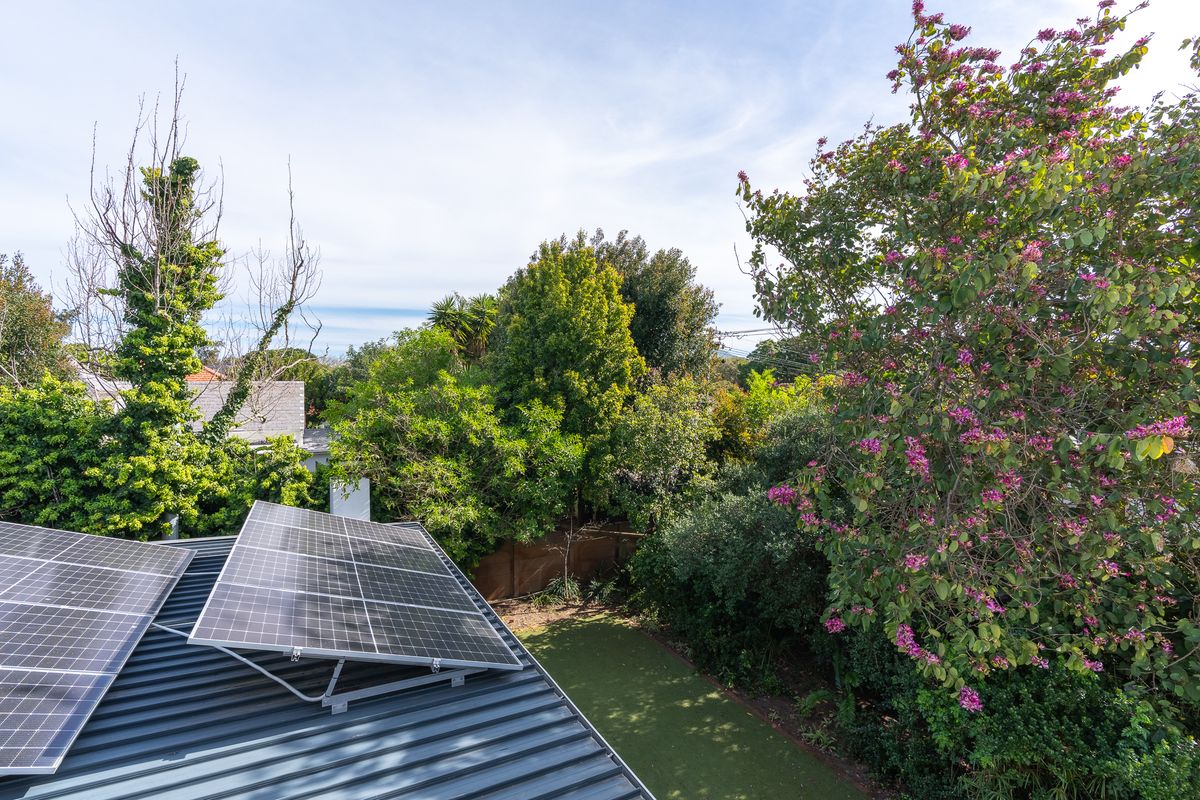 Aerial view of the property roof featuring installed solar panels, overlooking a lush garden with mature trees and artificial lawn.