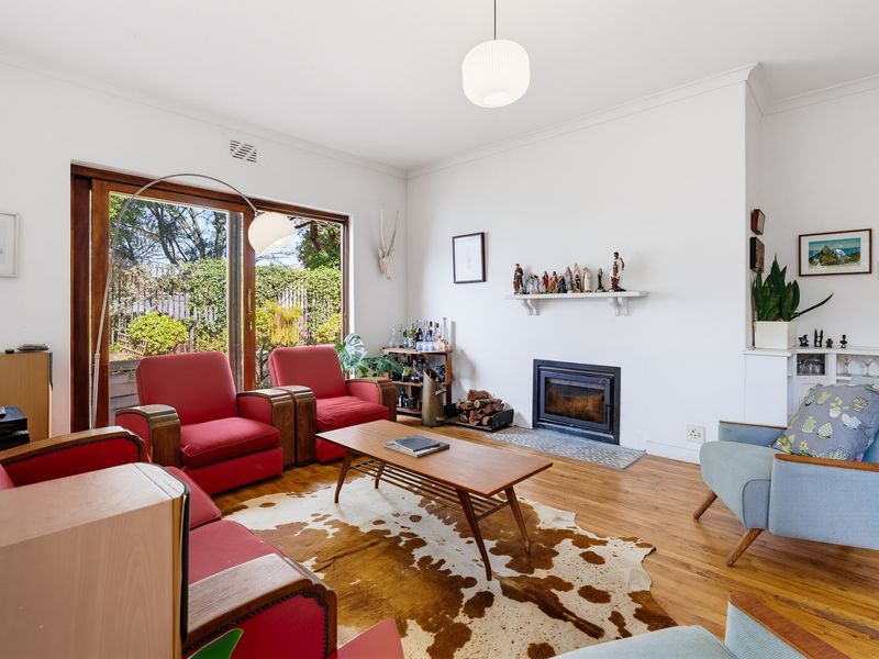 A bright living room featuring hardwood flooring, a built-in fireplace, and large sliding glass doors providing access to the garden.