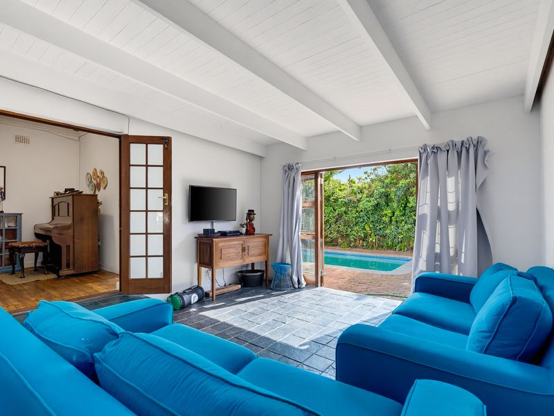 Bright living room featuring exposed beam ceilings, slate tile flooring, and direct access through french doors to the outdoor pool area.