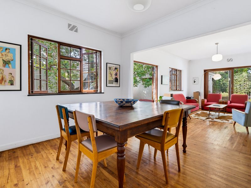 Open-plan living and dining area featuring polished timber flooring, classic casement windows, and seamless access to the outdoor space through sliding glass doors.