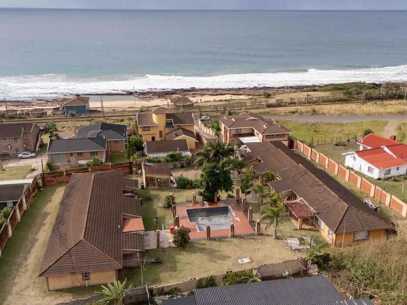 Aerial view of a coastal residential property featuring a swimming pool, tiled roof structures, and a large garden area near the ocean.
