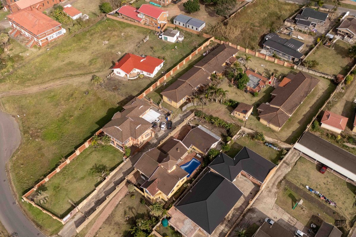 Aerial view of a residential property featuring a swimming pool, tiled roofing, and surrounding boundary walls within a suburban neighborhood setting.