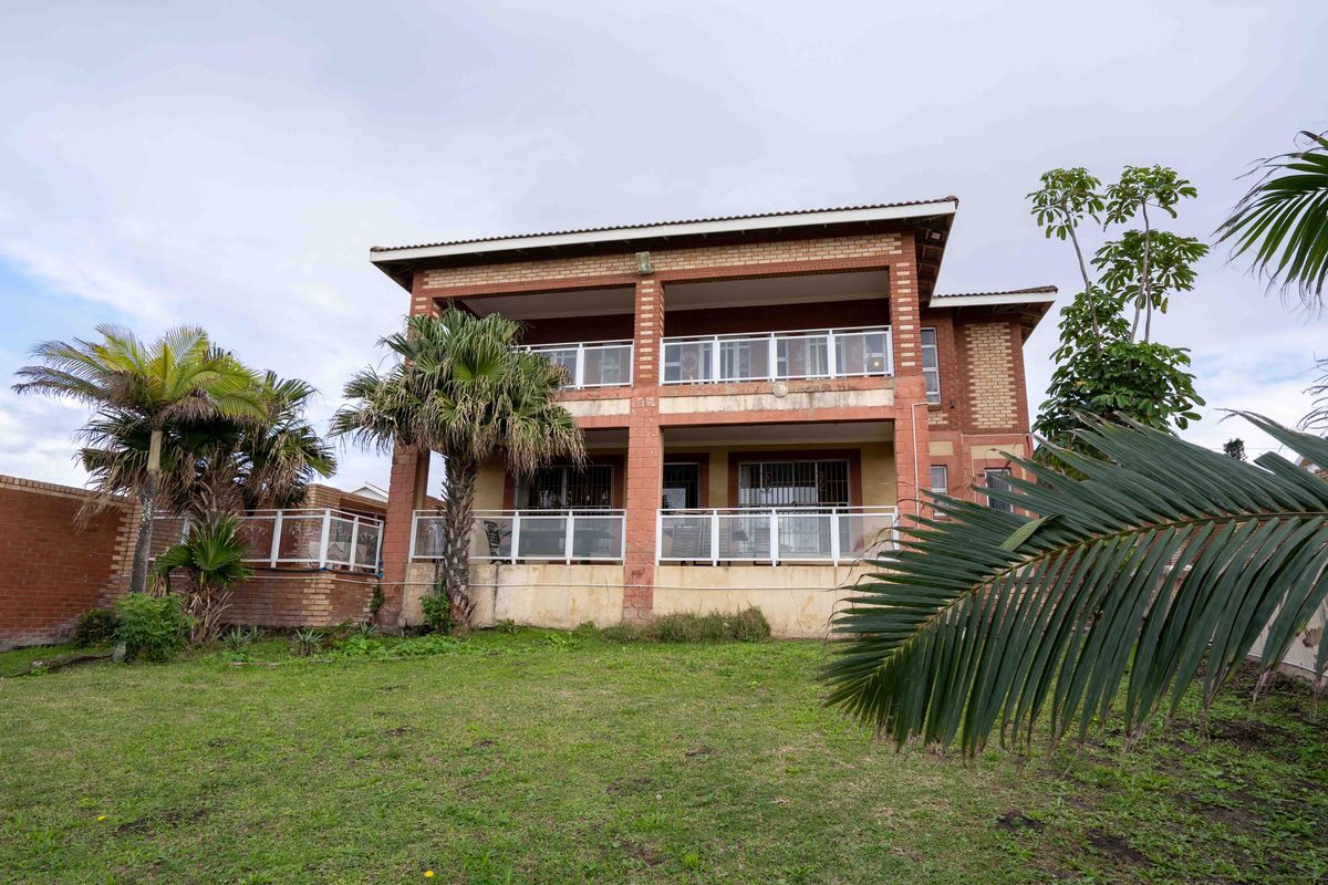 Rear view of a double-story brick house featuring covered balconies with metal railings and a spacious lawn area.