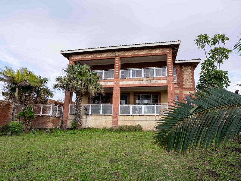 Rear view of a double-story brick house featuring covered balconies with metal railings and a spacious lawn area.