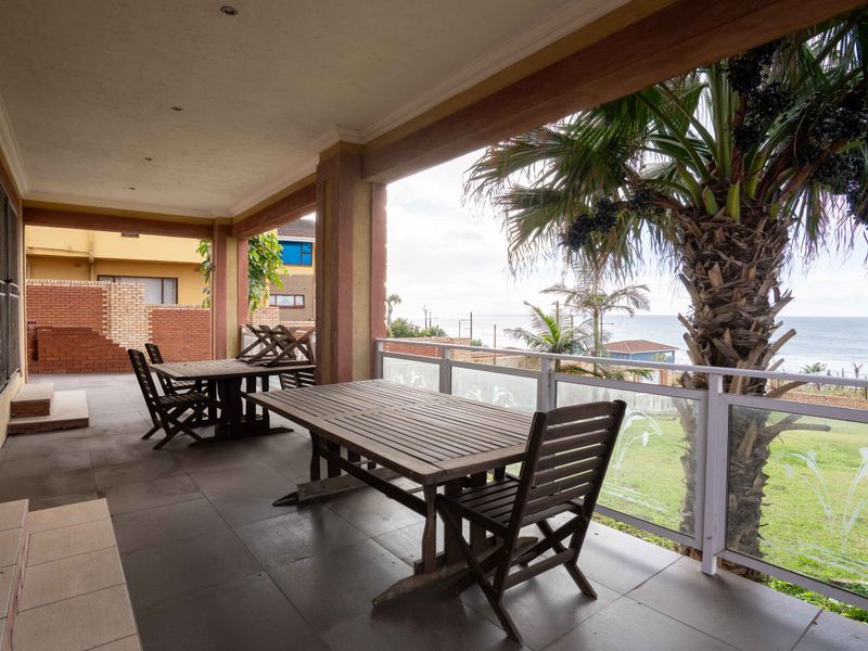 A spacious covered patio featuring tiled flooring and a glass balustrade, offering an outdoor entertainment area with views of the surrounding landscape.