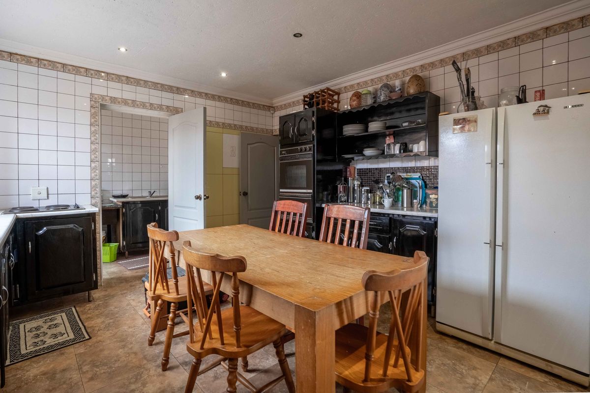 A functional kitchen featuring built-in cabinetry, an integrated oven, tiled splashbacks, and tiled flooring, with an adjacent scullery area visible.