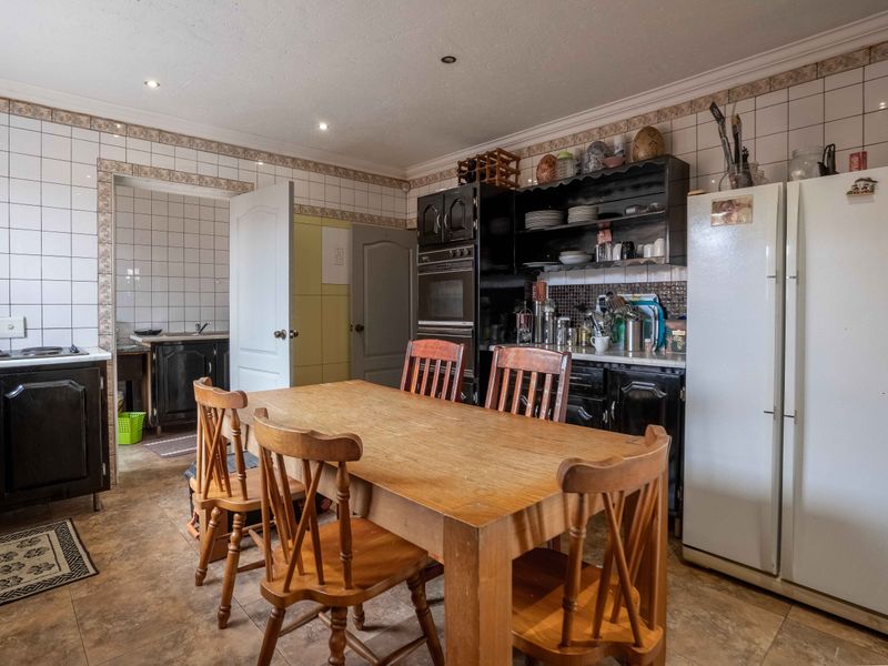 A functional kitchen featuring built-in cabinetry, an integrated oven, tiled splashbacks, and tiled flooring, with an adjacent scullery area visible.