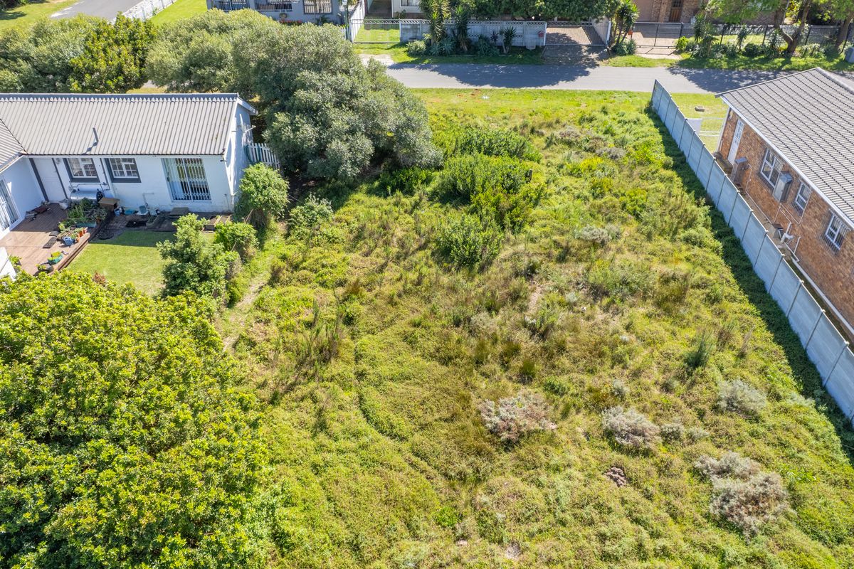Aerial view of a vacant residential plot featuring overgrown vegetation, bordered by existing residential properties and a precast concrete boundary wall.