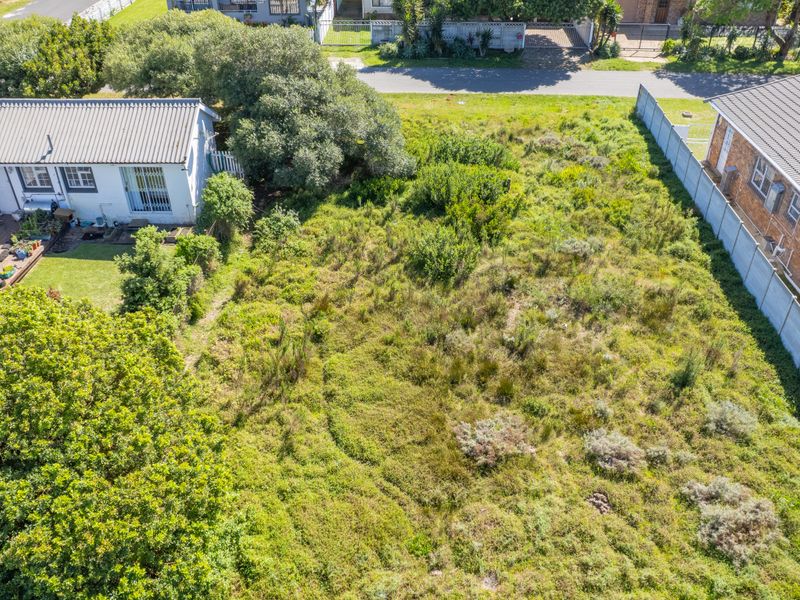 Aerial view of a vacant residential plot featuring overgrown vegetation, bordered by existing residential properties and a precast concrete boundary wall.