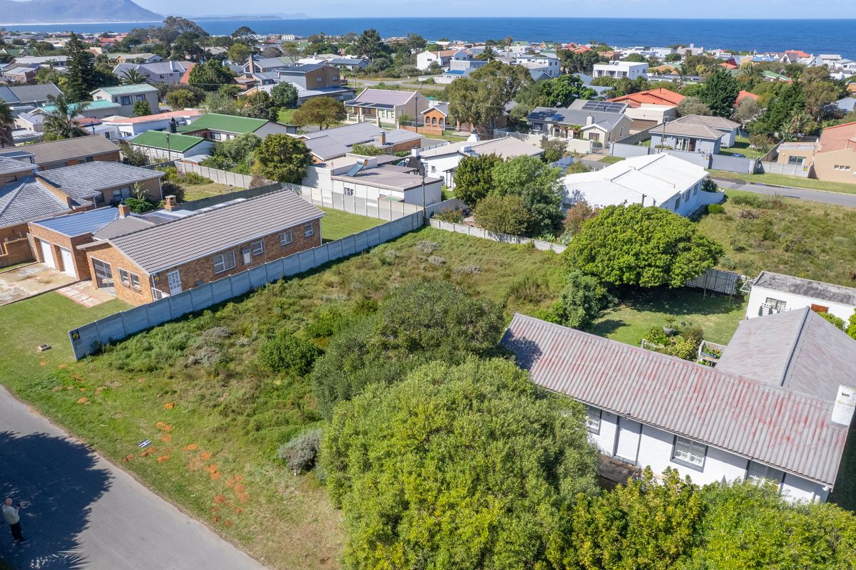 Aerial view of a vacant residential plot featuring mature trees and surrounding neighborhood infrastructure with ocean views in the distance.