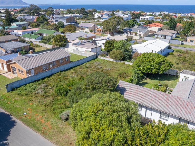 Aerial view of a vacant residential plot featuring mature trees and surrounding neighborhood infrastructure with ocean views in the distance.