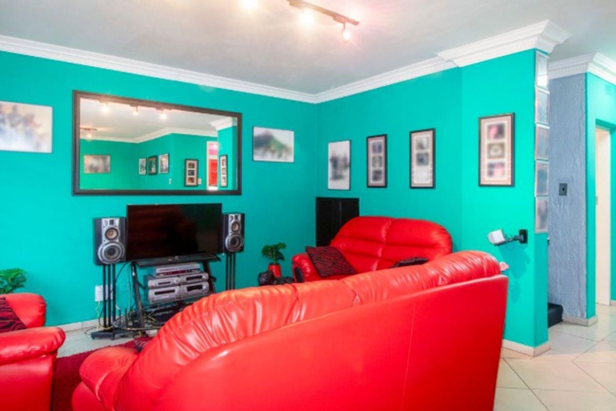 A living room featuring tiled flooring, crown molding, and track lighting, currently finished with vibrant wall paint.