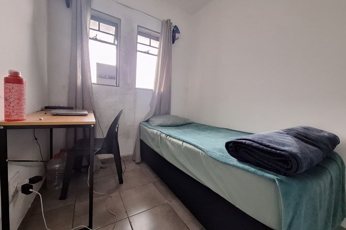 A compact bedroom featuring tiled flooring and dual casement windows, showing signs of wear on the wall surfaces.