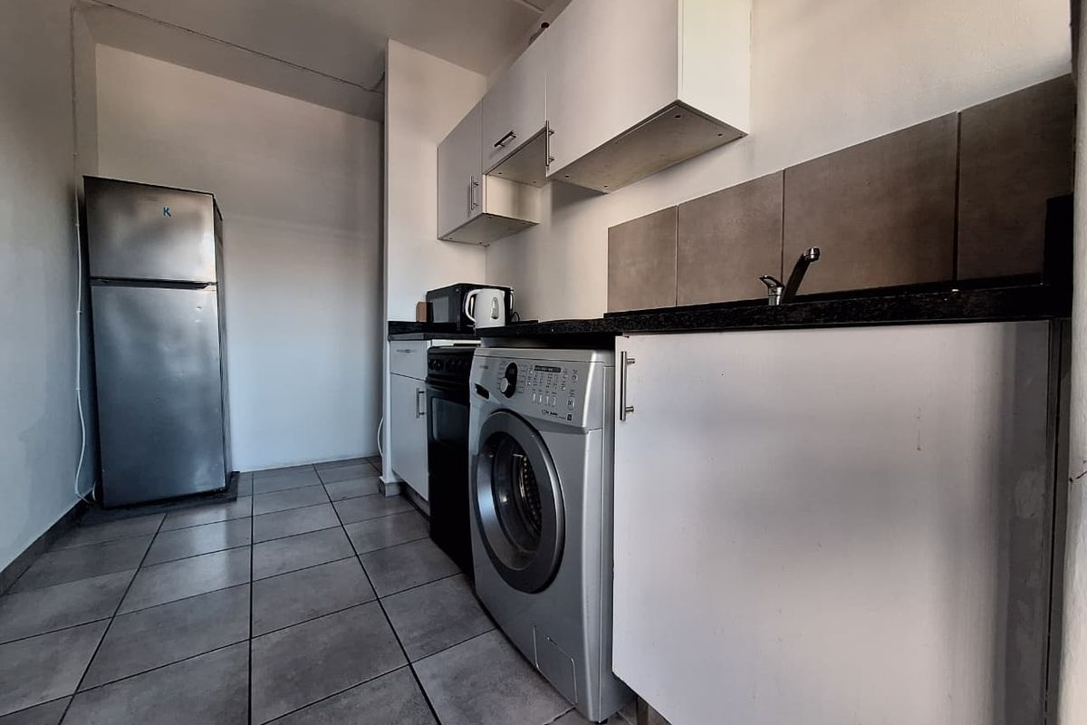 Compact kitchen featuring white cabinetry, dark stone countertops, tiled backsplash, and tiled flooring, providing a functional space for meal preparation.