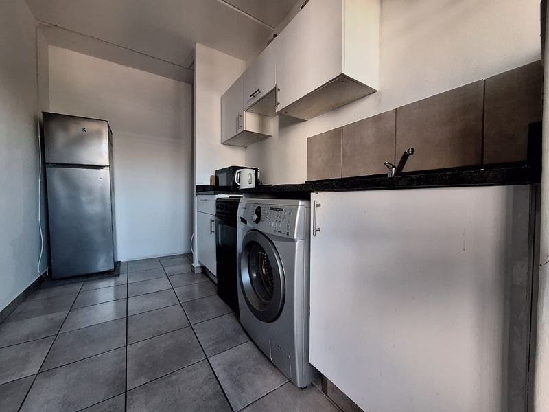 Compact kitchen featuring white cabinetry, dark stone countertops, tiled backsplash, and tiled flooring, providing a functional space for meal preparation.