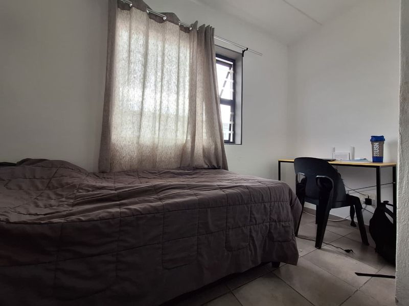 A functional bedroom featuring tiled flooring and a window fitted with security bars, providing natural light and basic utility.