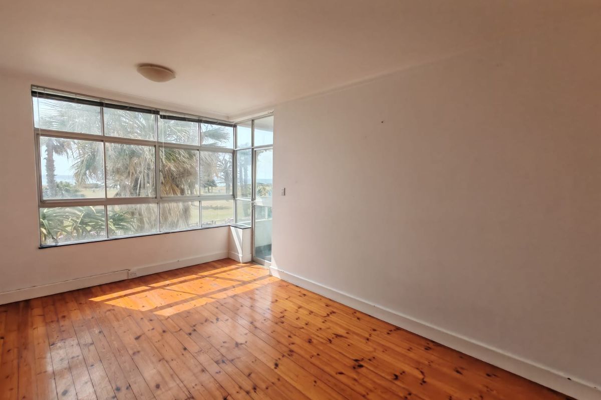 An empty living room featuring polished timber flooring and large corner windows that provide natural light and views.