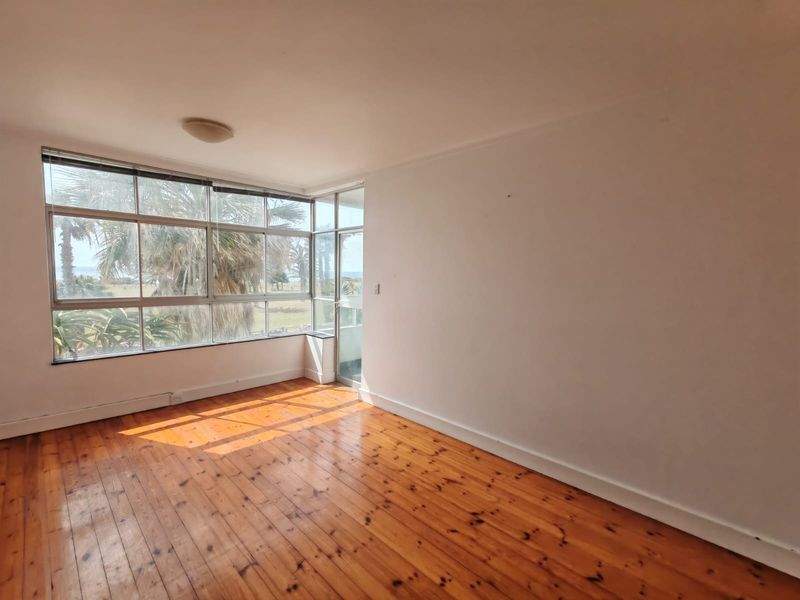 An empty living room featuring polished timber flooring and large corner windows that provide natural light and views.