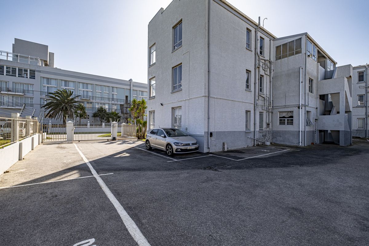 Rear exterior view of the apartment building showing the parking area, building facade, and external access points.